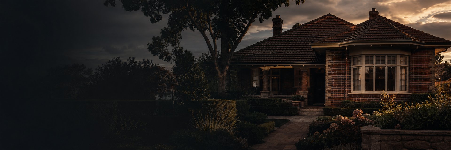 An established brick home at dusk, warm light in the windows