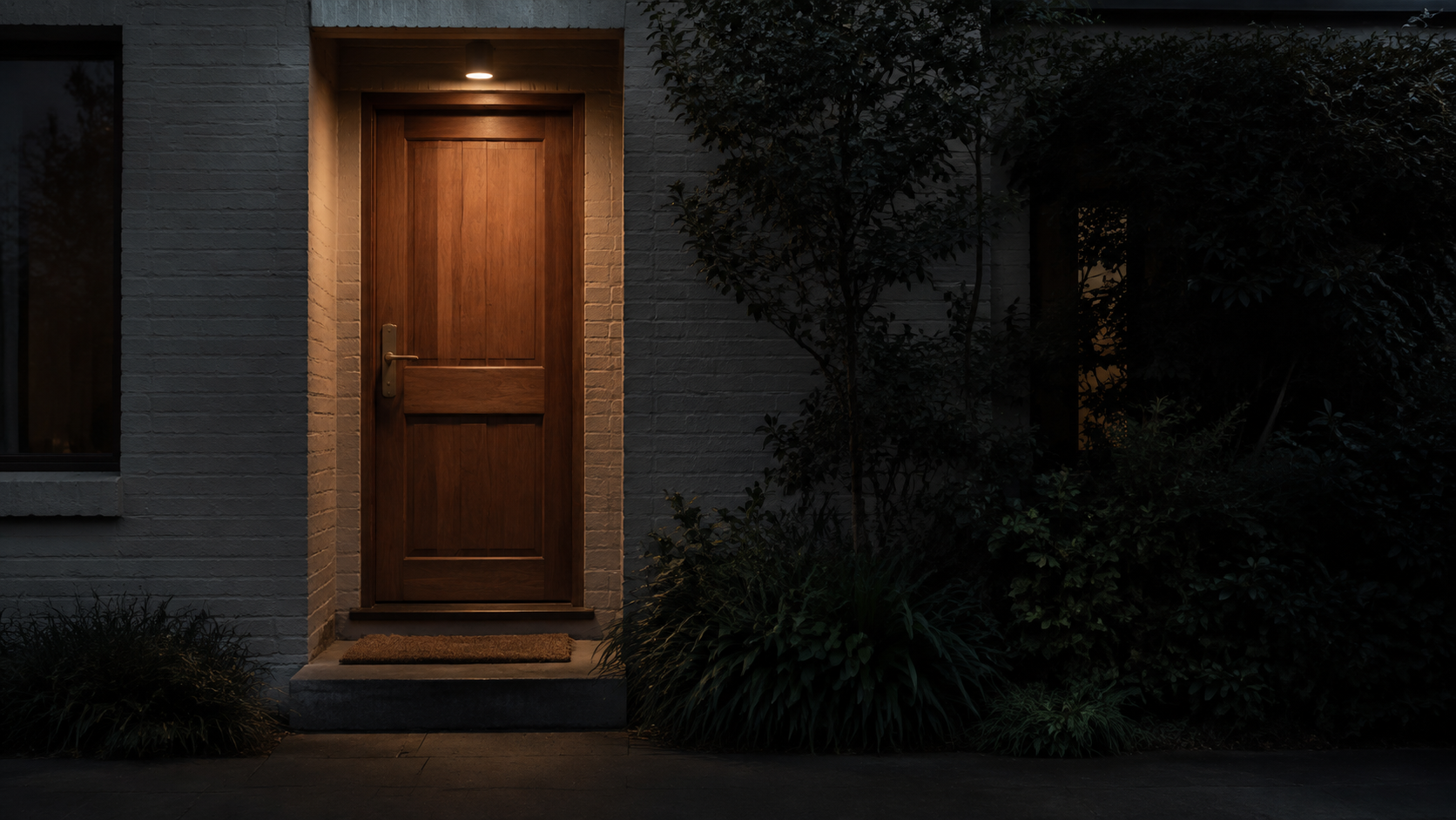 A timber front door at dusk, entry light on above the threshold